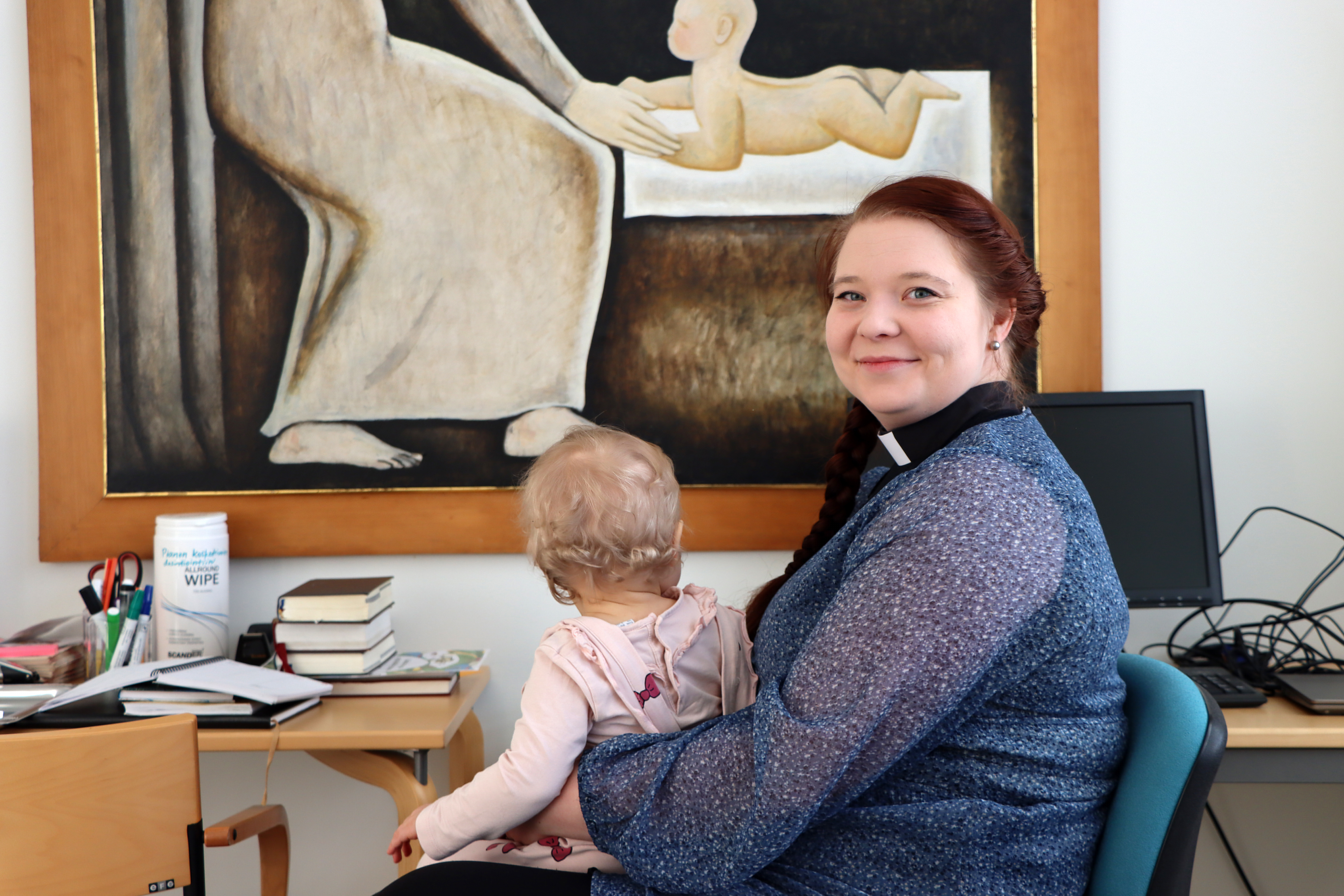 Pappi Elina Veima työpöytänsä ääressä. Sylissä pieni tytär selkä kohti kameraa.
