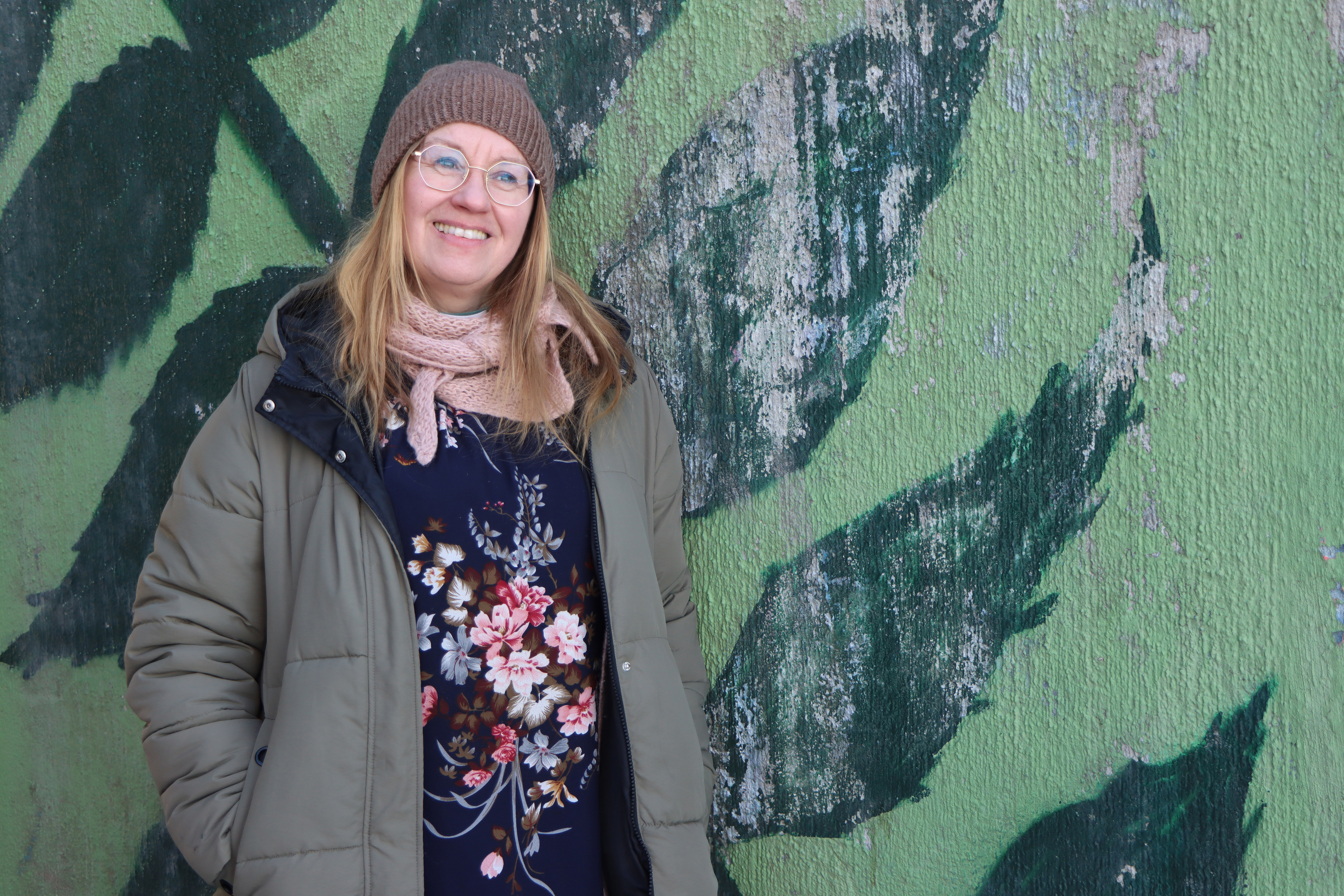 Diakoniatyöntekijä Päivi Kuivalainen. Taustalla vihreä graffitiseinä.