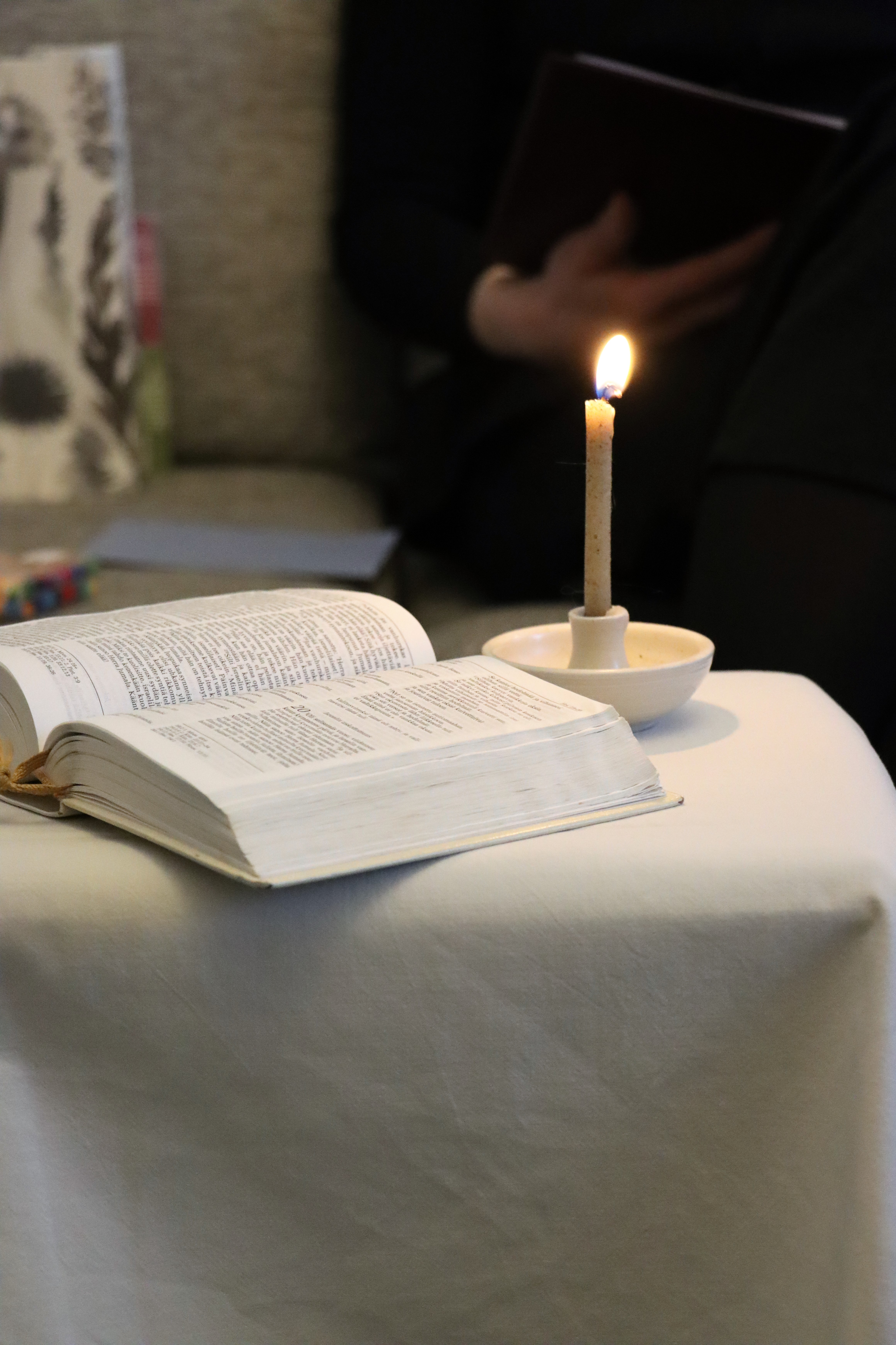 Auki oleva Raamattu pöydällä kynttilän vieressä.