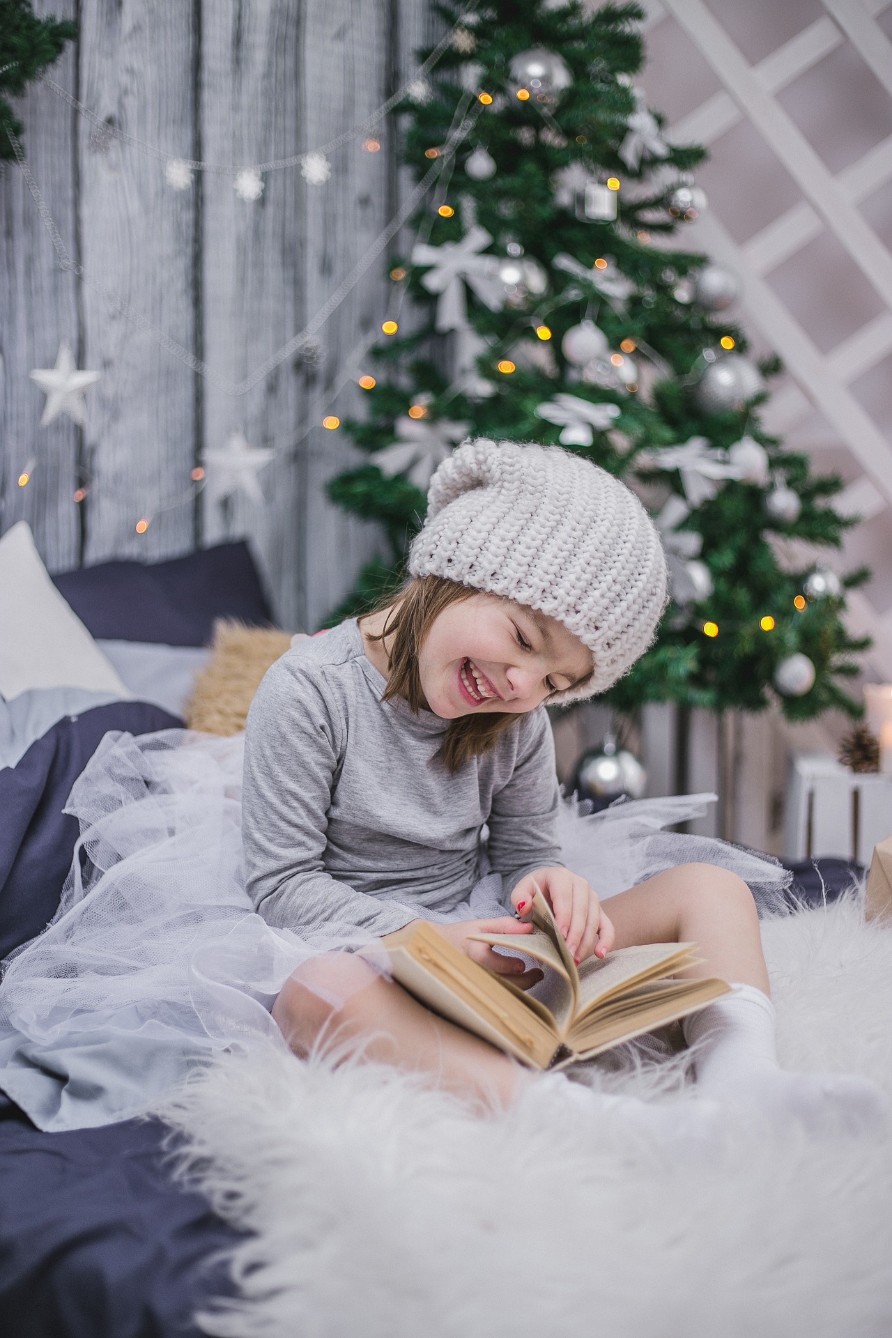 Lapsi selaa kirjan sivuja hymyssä suin. Taustalla joulukuusi ja lahjapaketti.