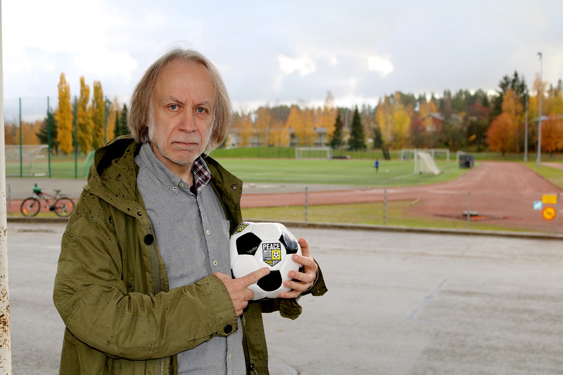 Pastori Arto Köykkä jalkapallo kainalossa. Taustalla häämöttää Pirkkalan keskuskenttä.