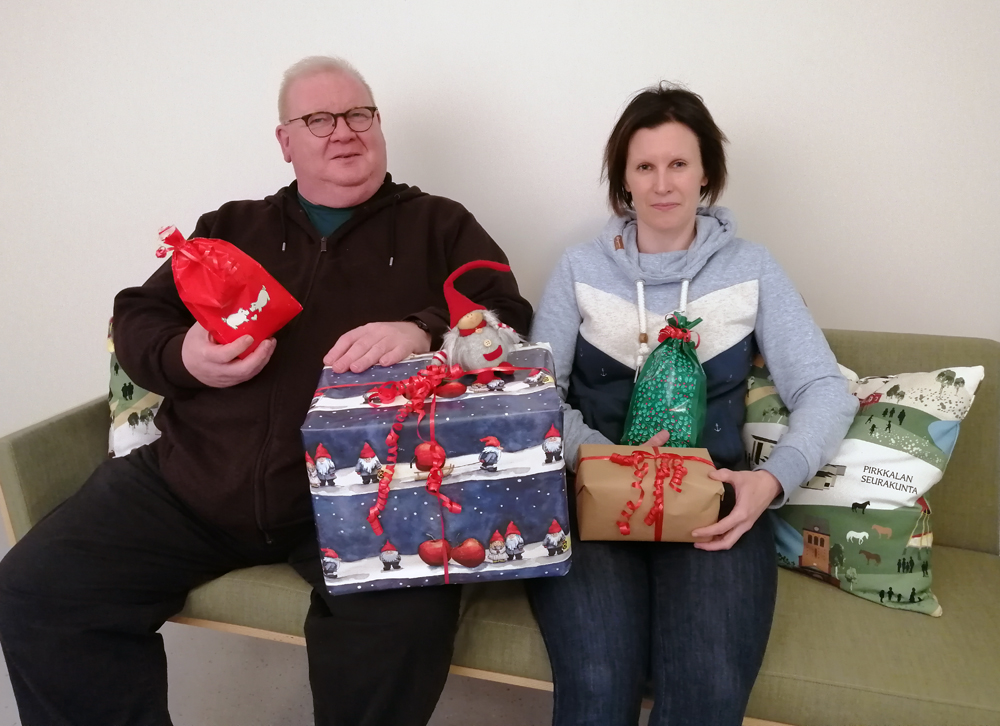 Diakoniatyöntekijät Jouni Kivimaa ja Petra Pajamäki sohvalla joululahjakeräyksen lahjapakettien kanssa.