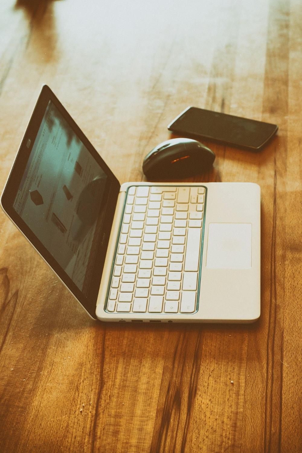 Tietokone, hiiri ja kännykkä pöydällä.